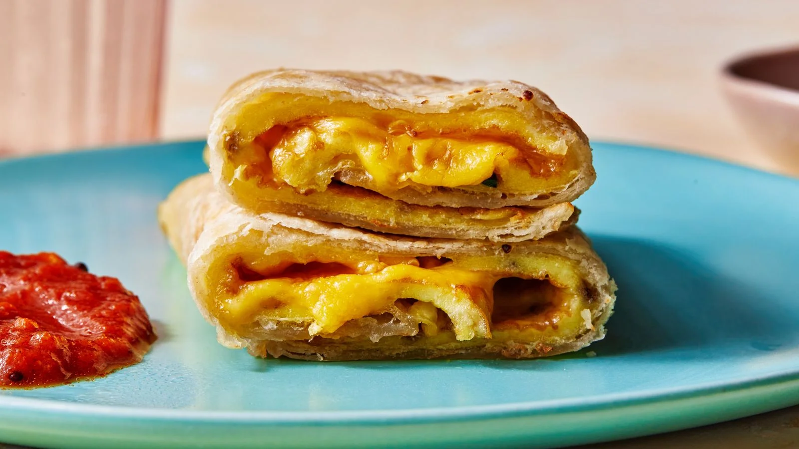 Straighton shot of a roti omelet rollup with sambal oelek on the side and american cheeze oozing out