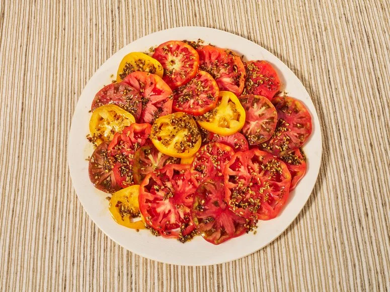 Brown Butter Tomatoes beautifully stacked on a white plate placed on a striped surface