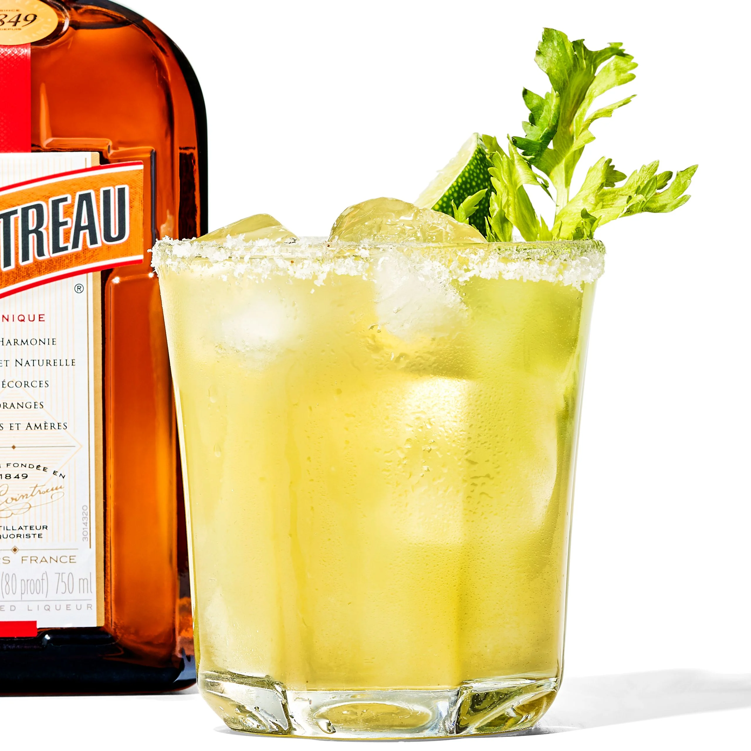 A rocks glass with a bright green margarita garnished with celery leaves.