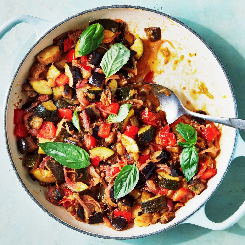 One-pot ratatouille with eggplant zucchini tomatoes red onion and bell pepper garnished with fresh basil in a shallow dish.